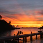 a group of people standing on a dock at sunset